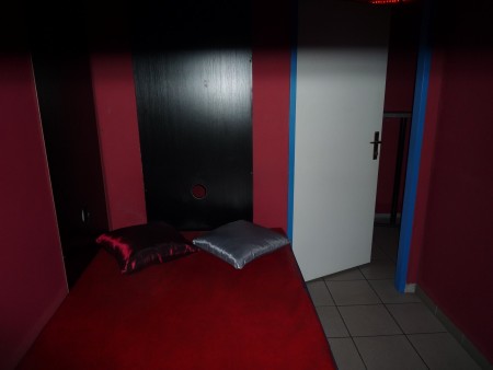 Liege mit rotem Bezug vor einer dunklen Wand mit einer runden Öffnung.