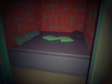 Kleiner Raum mit einer breiten Liege und Kissen. Die Fotoseite nennt ihn Paarzimmer.